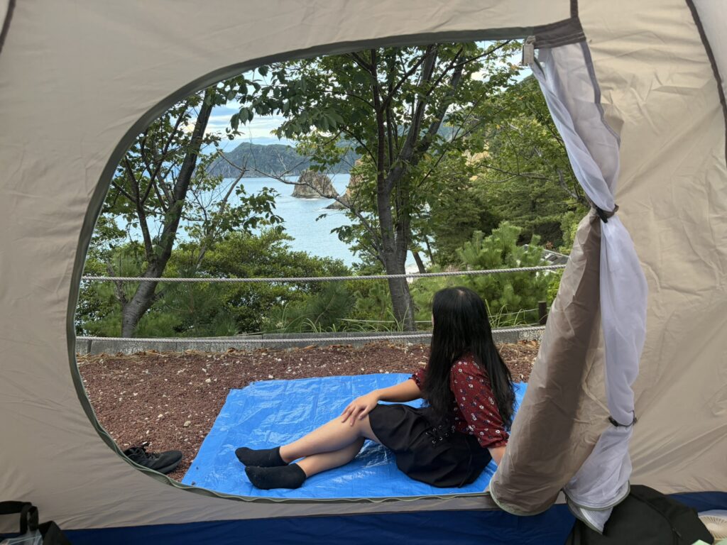 Relaxing inside a tent with a view of the ocean and cliffs at Camp Koganezaki.