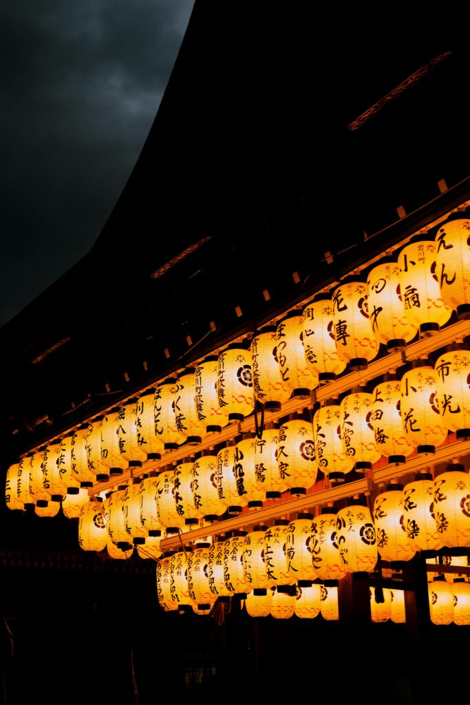 Rows of traditional Japanese lanterns glowing warmly at night during a summer festival.