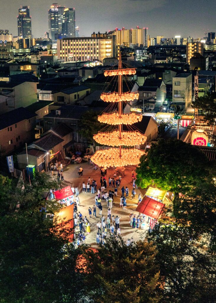 Person dancing with a fan beneath glowing red lanterns at a Japanese Obon festival.