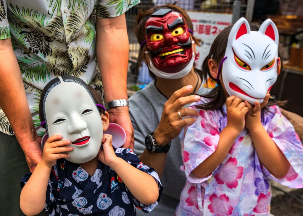 Children and adults wearing traditional Japanese festival masks while dressed in summer clothing and yukata.