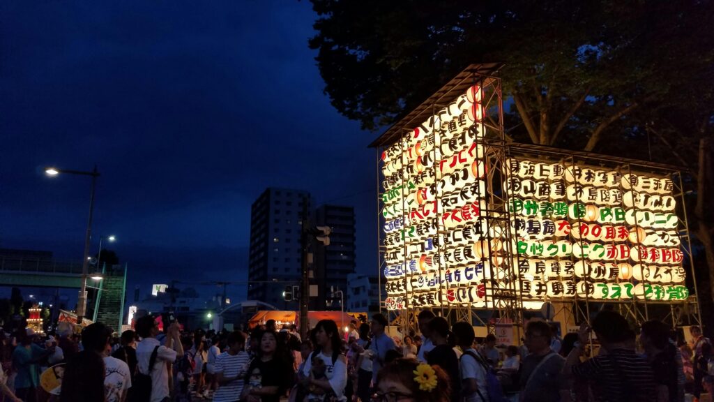 Crowded Japanese summer festival at night with a large illuminated lantern display.
