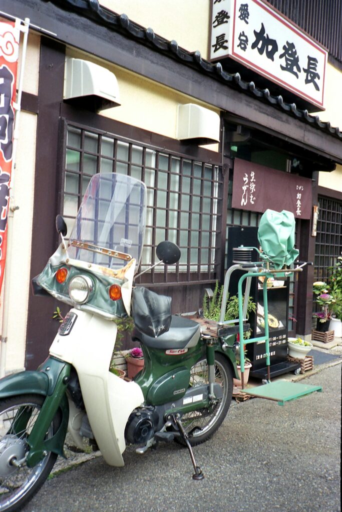 Retro Honda motorbike parked outside a traditional Japanese storefront.