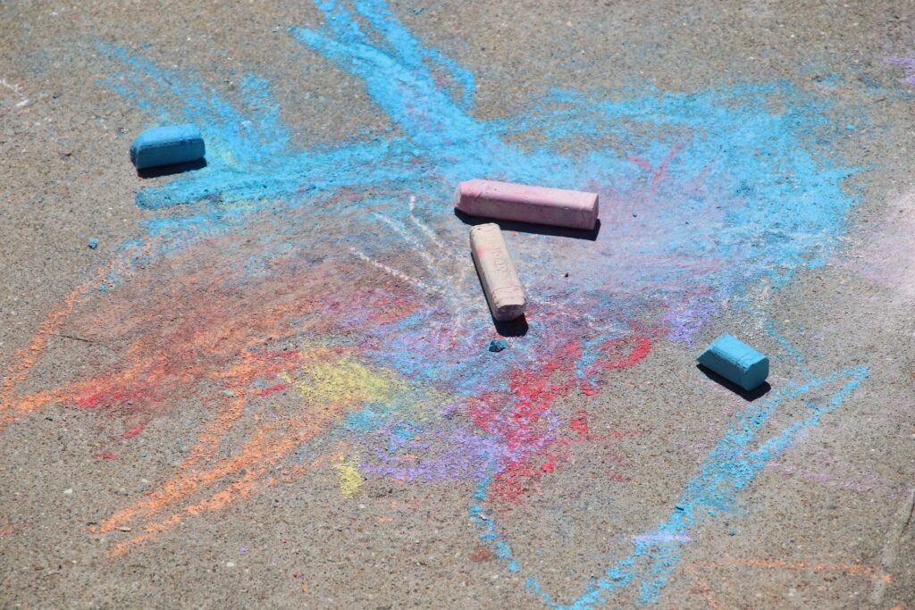 Colorful sidewalk chalk drawings and chalk pieces on the ground.
