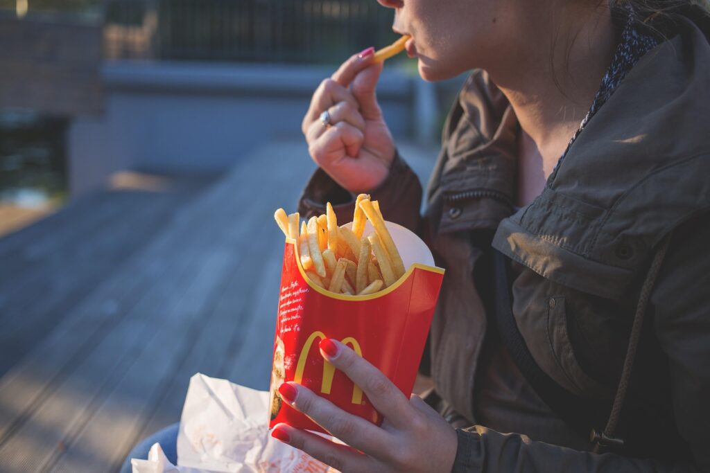 Woman eating French fries from a fast-food container outdoors.