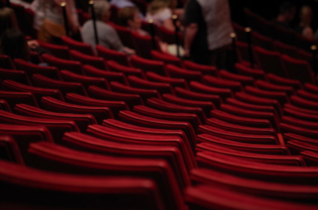 Rows of red upholstered seats inside a theater auditorium, offering a glimpse of the seating arrangement for a live musical performance.