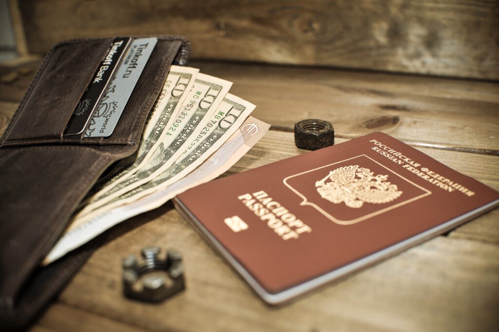 Passport, wallet and cash placed on a wooden table, representing important travel documents and valuables.