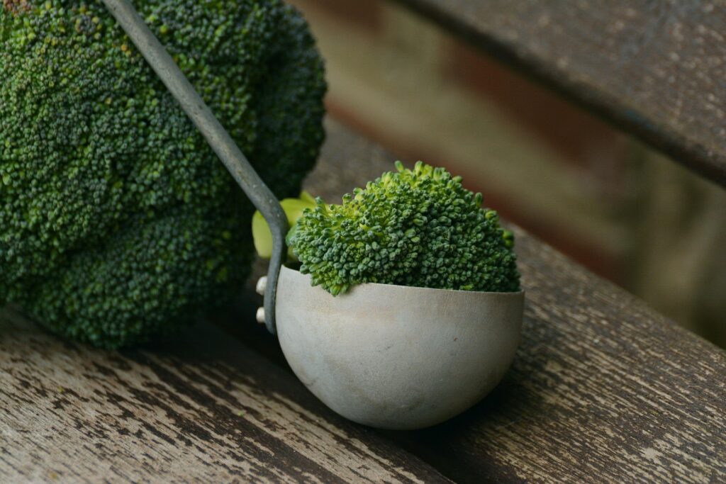 Fresh broccoli florets in a metal measuring cup on a wooden surface.