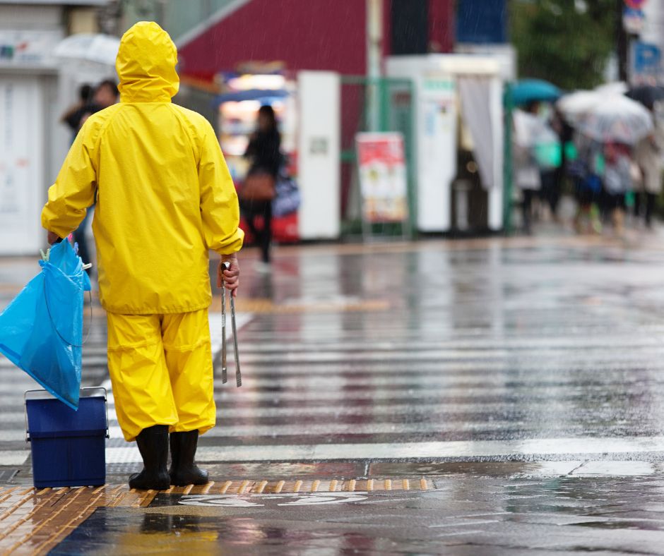 A person wearing a bright yellow raincoat and boots stands on a wet street in Japan during heavy rain.