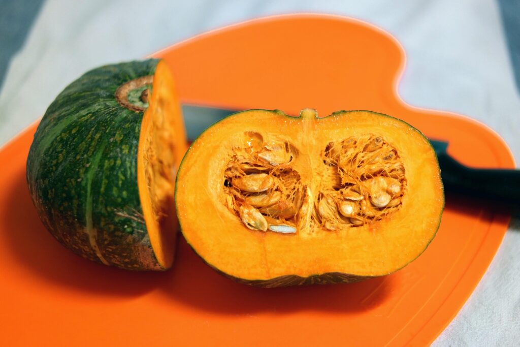 Fresh kabocha pumpkin cut in half, showing its bright orange flesh and seeds.