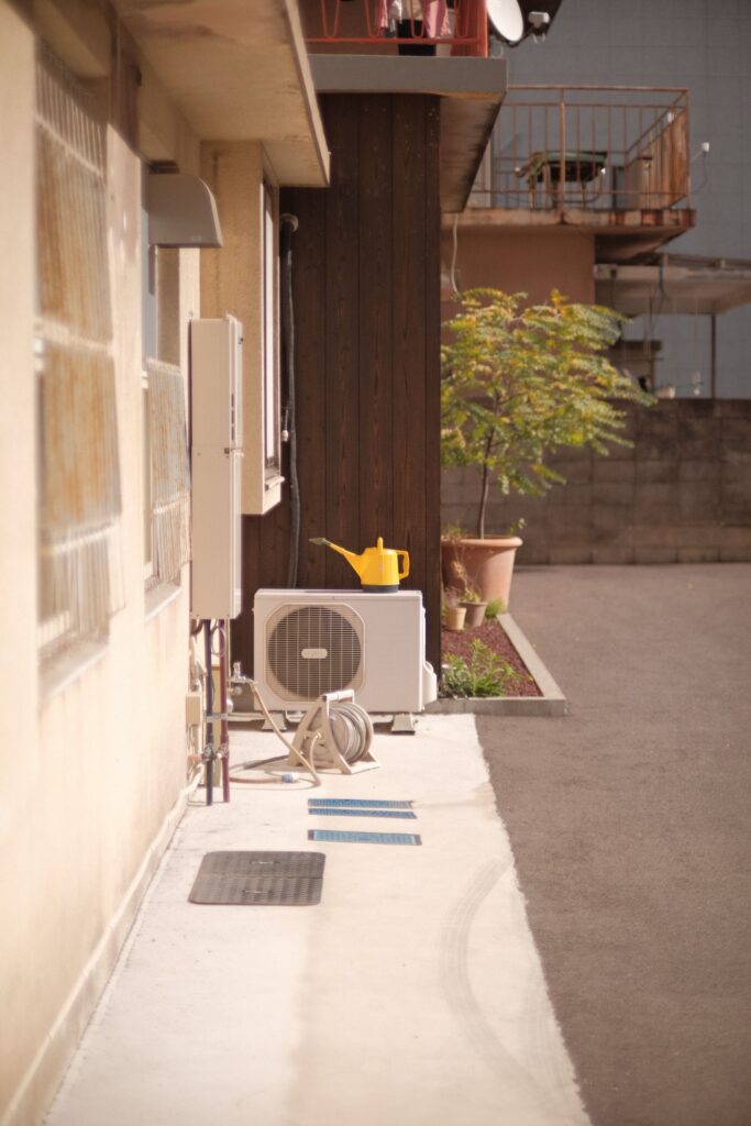 A wall-mounted outdoor water heater installed beside an air conditioning unit along the exterior of a residential building.