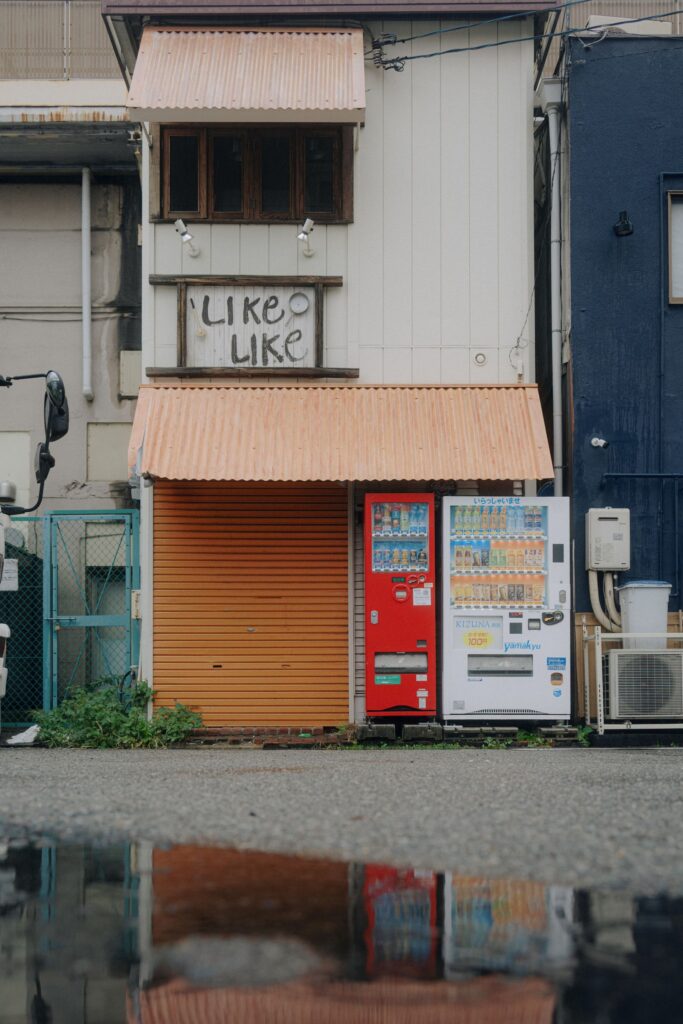 A white outdoor water heater mounted on the exterior wall of a Japanese building beside two vending machines.