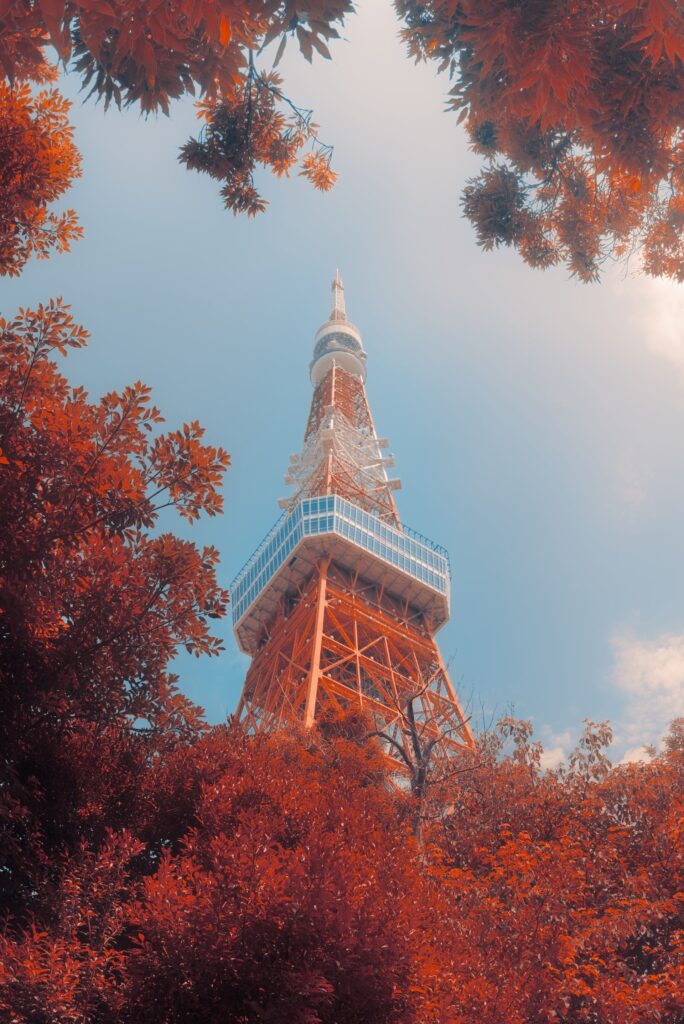 Tokyo Tower framed by vivid red and orange autumn foliage against a blue sky.