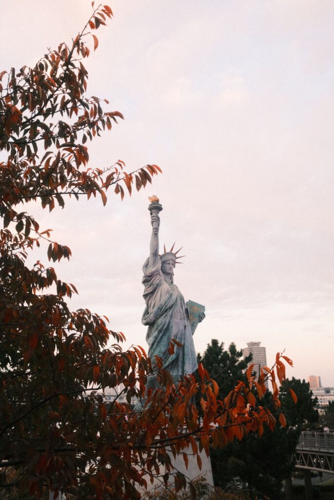 Statue of Liberty replica framed by reddish-brown autumn leaves in Odaiba, Tokyo.