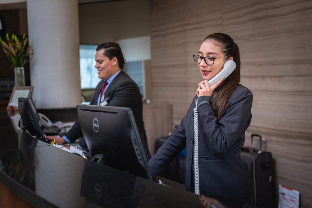 Hotel reception staff assisting guests at the front desk, where travelers may ask about luggage storage before check-in.