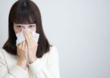 Woman holding tissues to her nose while experiencing seasonal allergy symptoms.