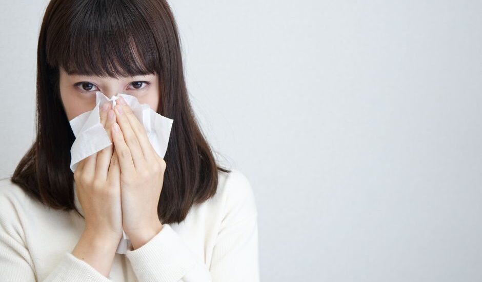 Woman holding tissues to her nose while experiencing seasonal allergy symptoms.