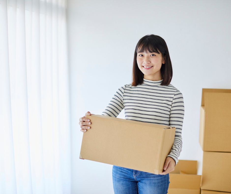 Woman using a laptop while surrounded by cardboard boxes, planning and organizing her move to a new apartment.