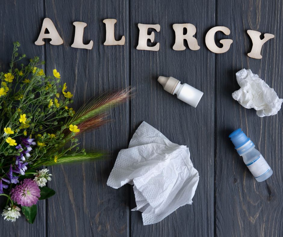 Allergy concept with flowers, tissues, nasal sprays, and the word “ALLERGY” on a dark wooden background.