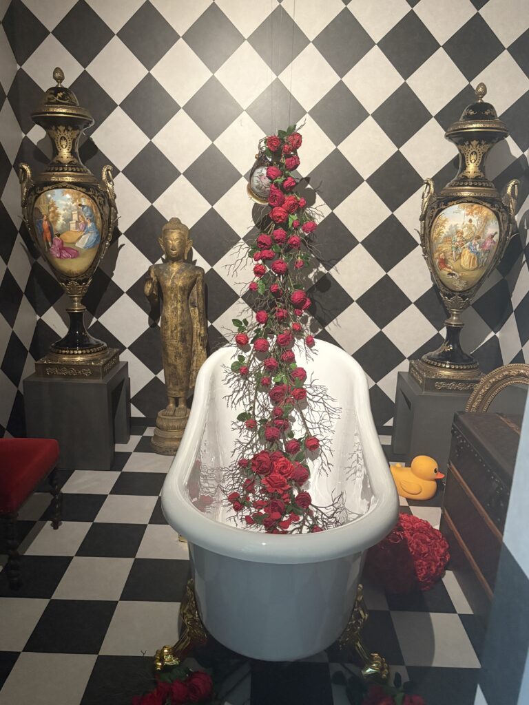 Decorative bathtub filled with red roses, surrounded by vintage European-style vases and black-and-white checkered walls inside Kitano Ijinkan.