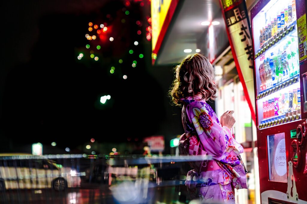 Woman wearing a yukata beside a vending machine at night in Japan, representing everyday life for residents in Japan.
