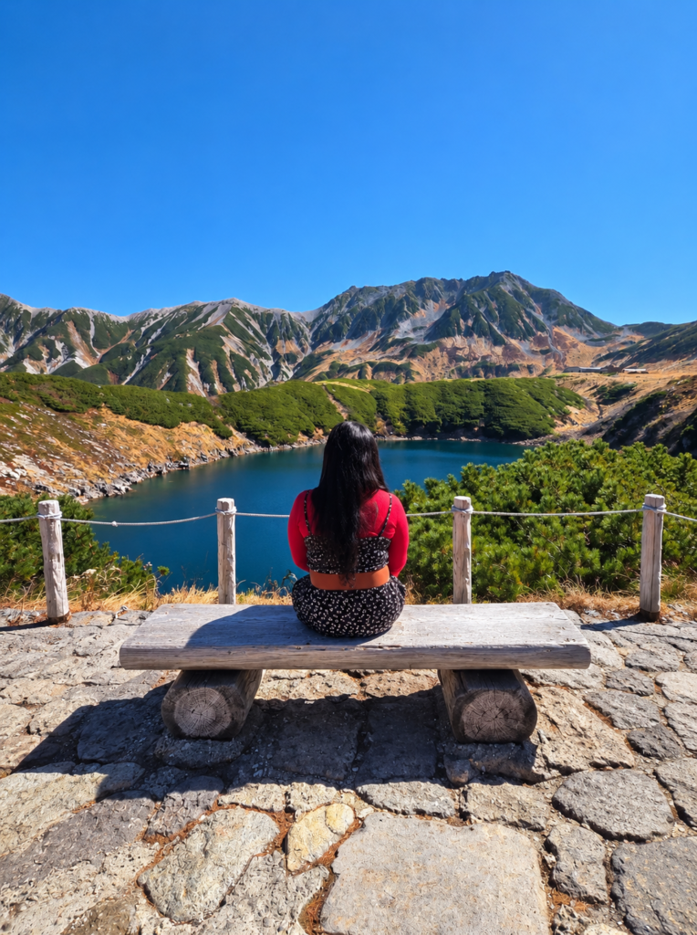 Traveler sitting on a wooden bench overlooking the beautiful Mikurigaike Pond and majestic mountain peaks at Murodo along the Tateyama Kurobe Alpine Route.