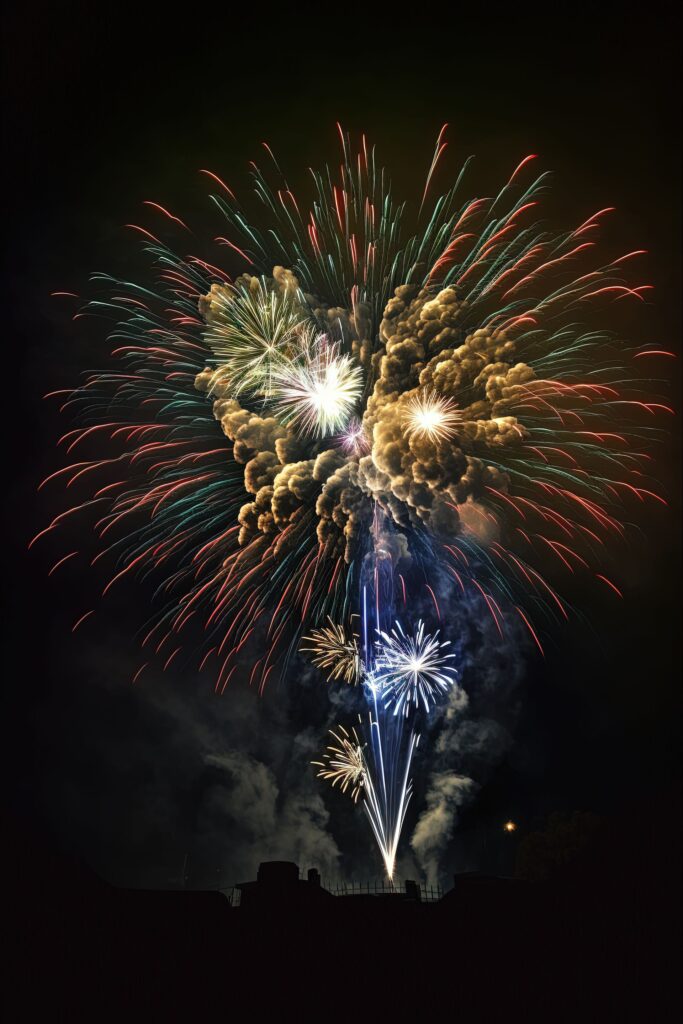 Colorful fireworks explode against a dark night sky, with bright white, green, and red sparks surrounded by clouds of smoke.