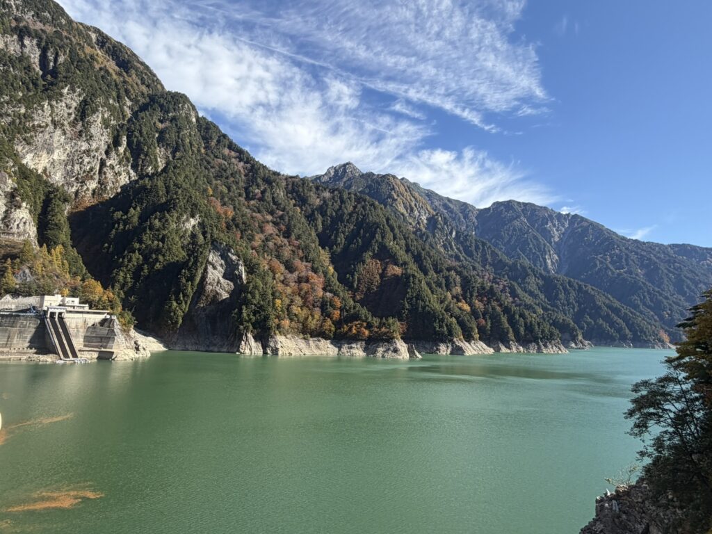 Beautiful turquoise waters of Lake Kurobe surrounded by towering mountains and colorful autumn foliage along the Tateyama Kurobe Alpine Route.