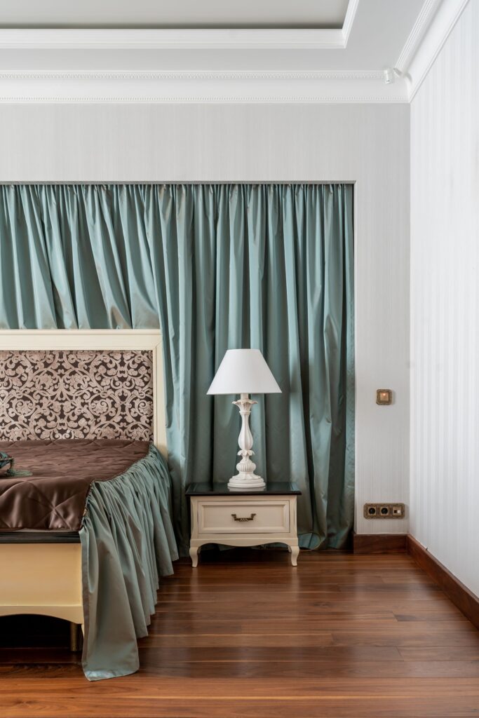 Thick floor-length curtains cover a bedroom window, demonstrating how heavy curtains can help reduce heat loss and keep rooms warmer during winter.