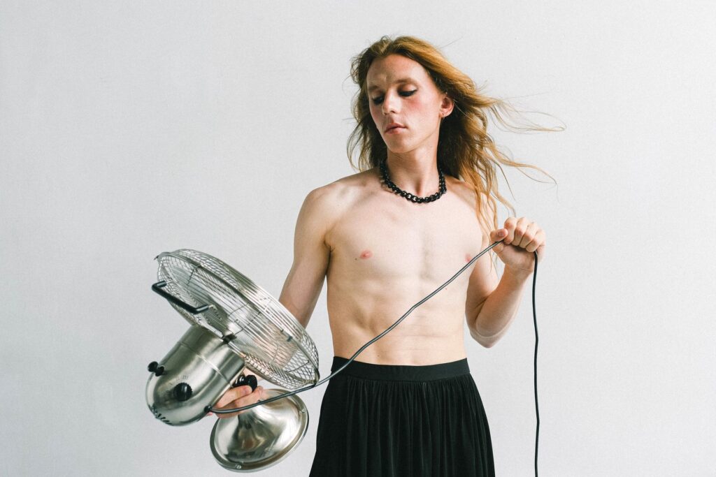 A person holding an electric fan to improve air circulation and distribute warm air throughout a room during winter.